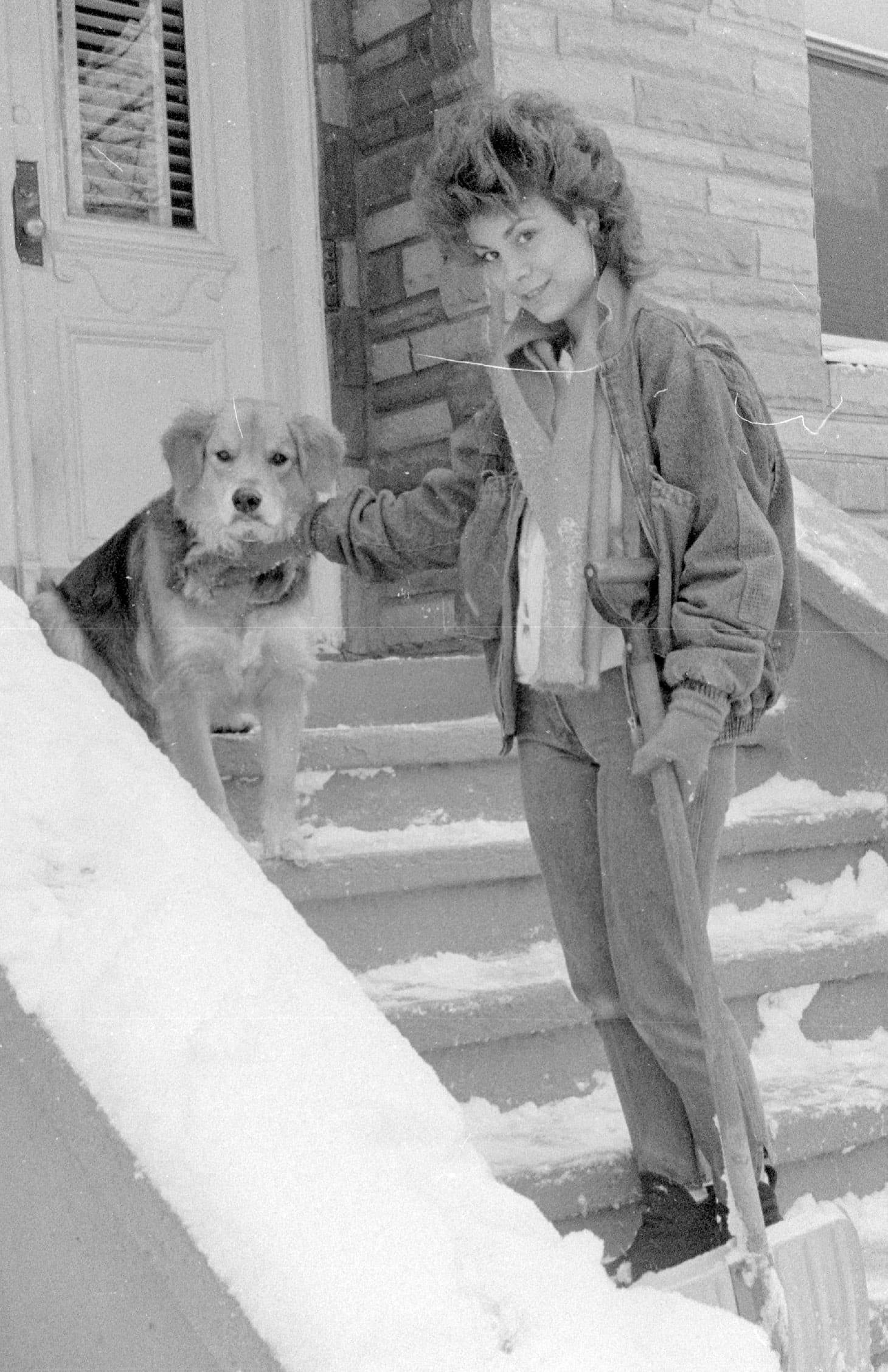 A woman and dog stand on snow-covered steps