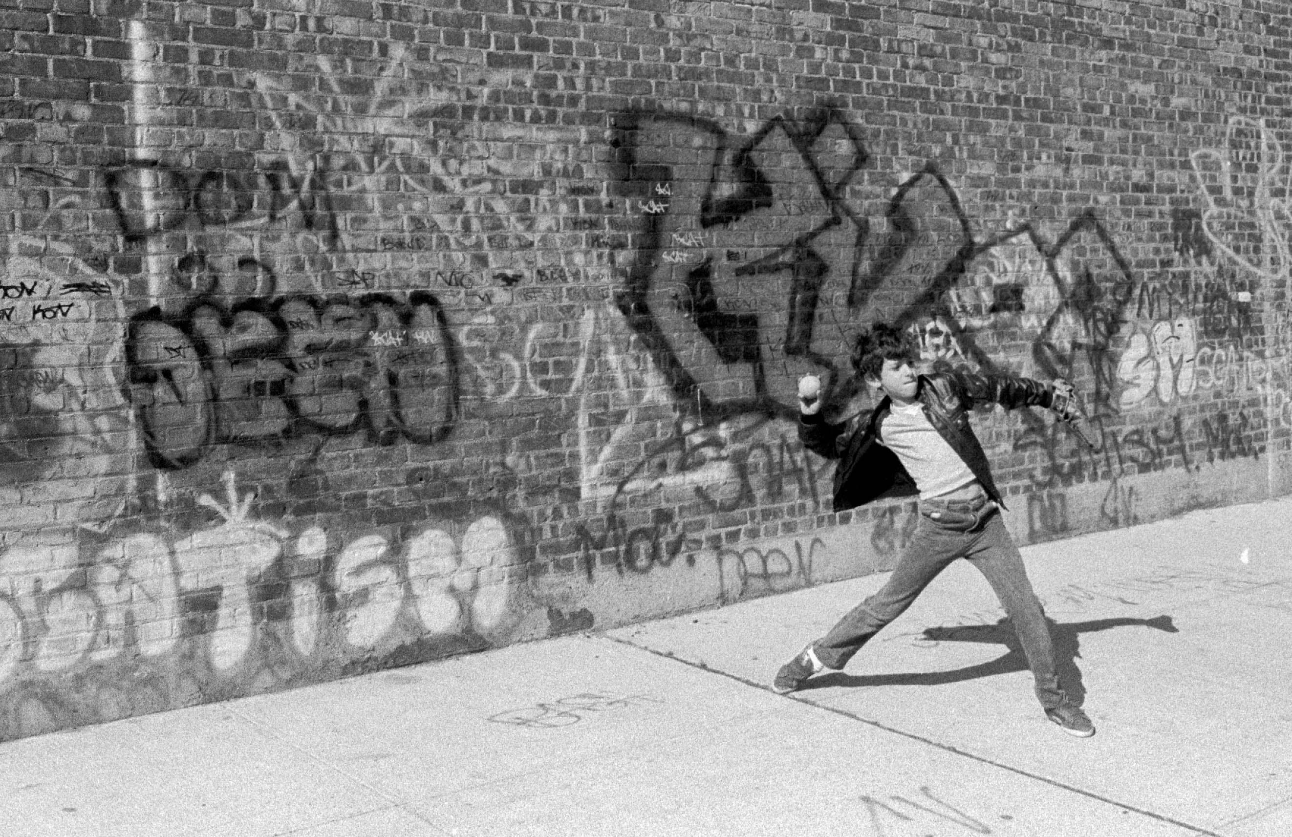 A dancer moves past a graffiti-covered brick wall