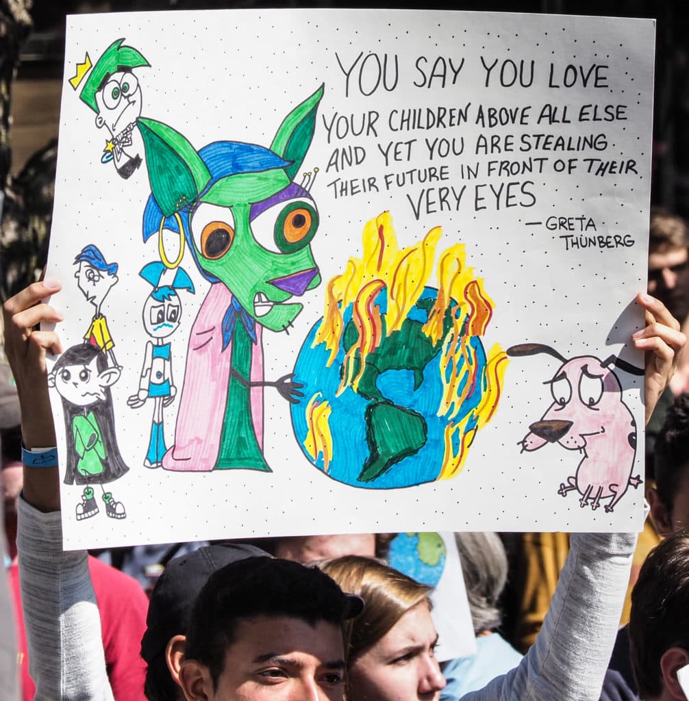 A climate strike participant holds an illustrated sign about protecting children’s future
